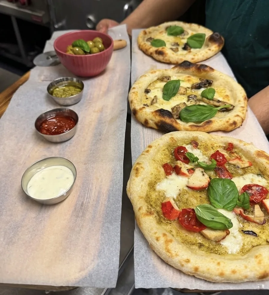 Kolme mini-pizzaa tarjolla dippejä ja marinoituja oliiveja — Three mini pizzas served with dips and marinated olives